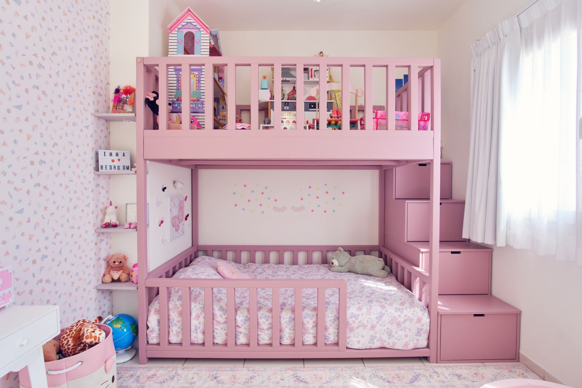 Compact pink children’s bedroom with custom bunk bed, wall shelving, and built-in staircase storage