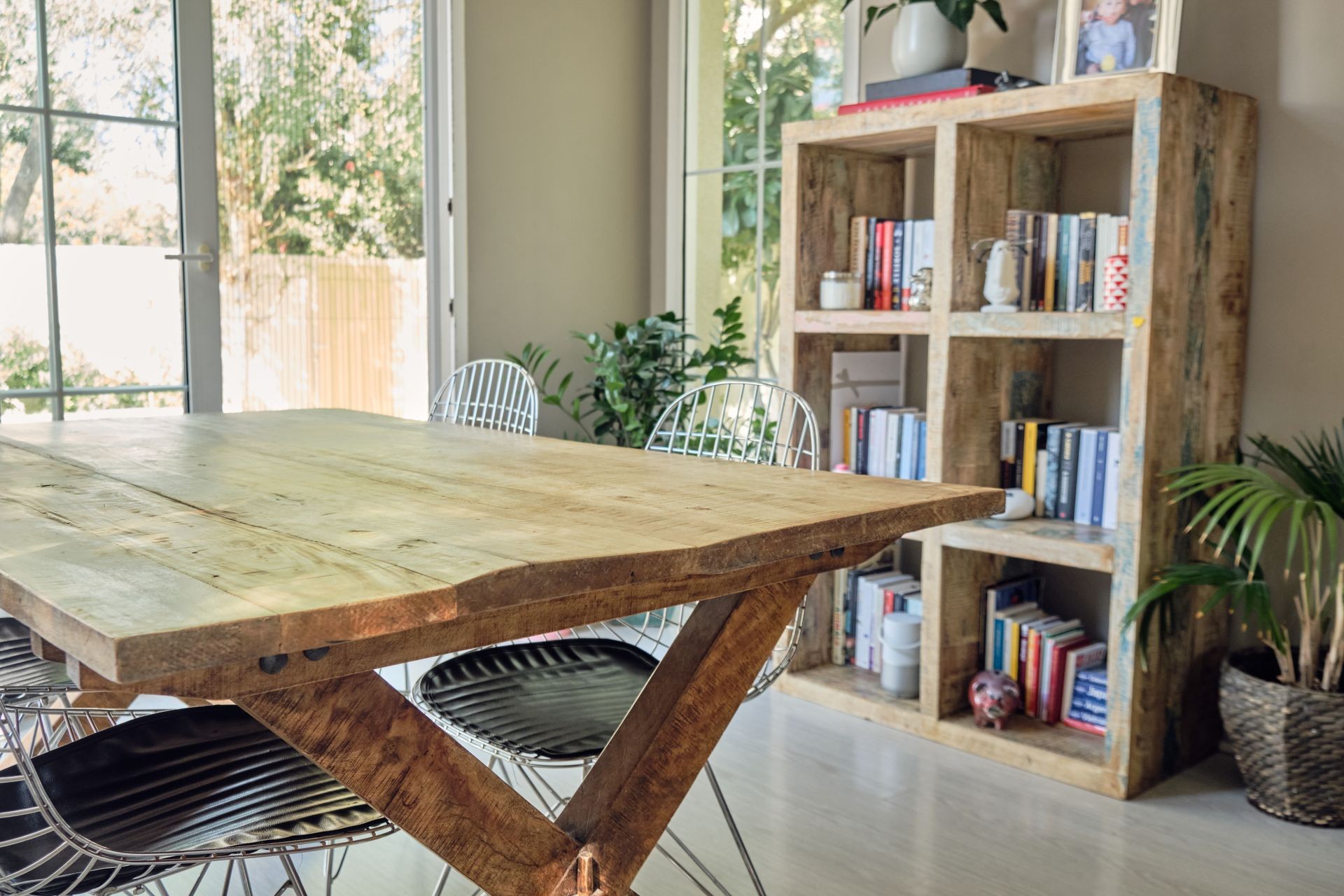 Rustic wood dining table with metal chairs and open bookshelf in a bright, modern interior