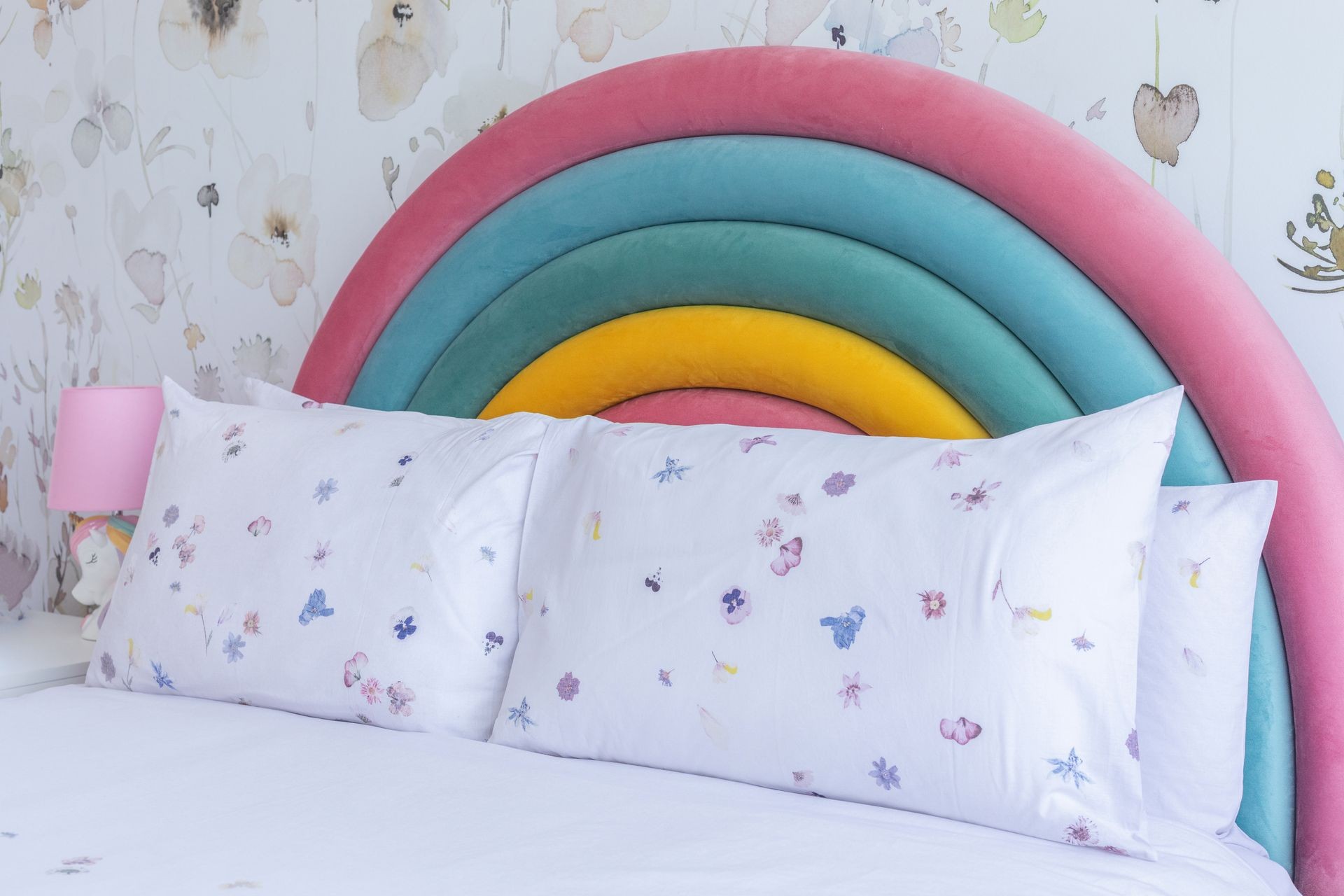 Colorful rainbow-themed headboard with floral-patterned pillows and pastel decor.