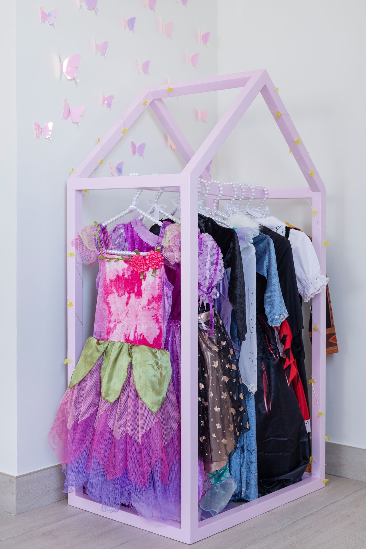 Children's costumes on hangers in a pink house-shaped rack with butterfly wall decorations.